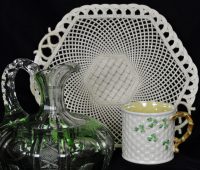 TFTV_March2020_Bellek and Cut Glass In the background is a white, woven porcelain cake plate; in the foreground left is a green and clear cut glass decanter; in the foreground right is a white porecelain cup with a weave pattern and green shamrock leaves