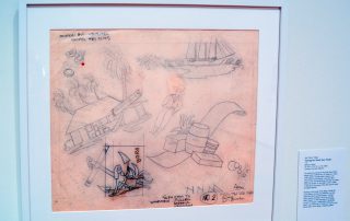 Original drawings on tracing paper showing a woman and a boat anchor, barrels of goods, a man in a straw hat, a hut with a sign that says "Trader Joe's", and a ship