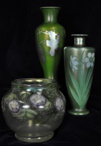 Three green vases. Two tall, one a smaller bowl. All have white flowers on them.