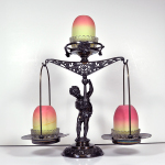 Lamp stand with a figure holding a scale with free-hanging scale baskets. The top of the scale and each basket hold a fairly lap base and shade.