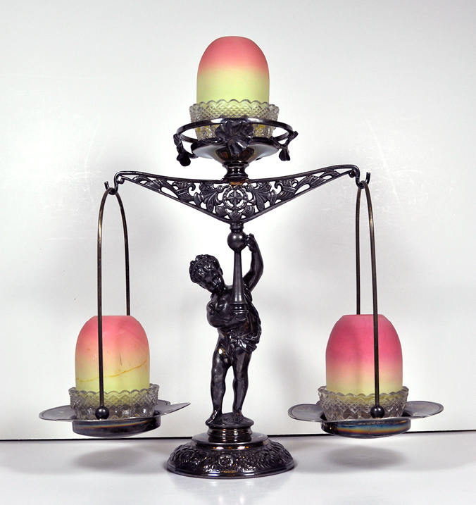 Lamp stand with a figure holding a scale with free-hanging scale baskets. The top of the scale and each basket hold a fairly lap base and shade.