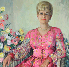 Portrait of Mrs. Irma F. Runyon in a pink dress with floral design, seated in a chair in a green room surrounded by bouquets of flowers.