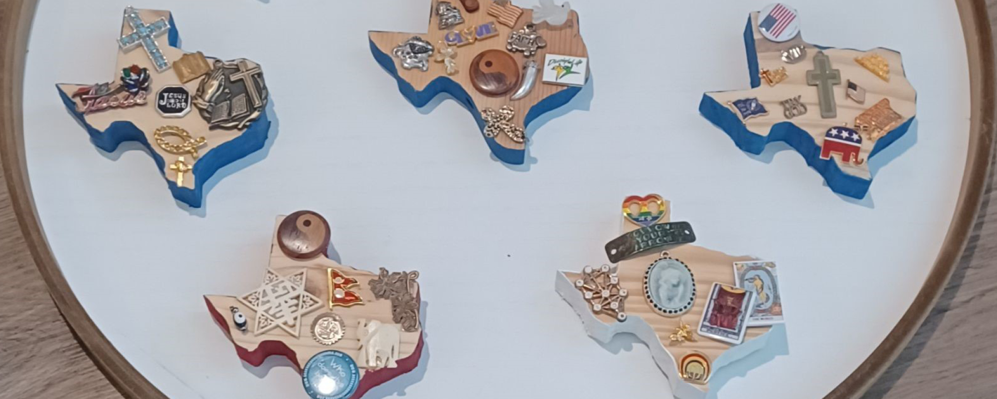 Wooden blocks each cut in the shape of Texas are adorned with small religious trinkets.