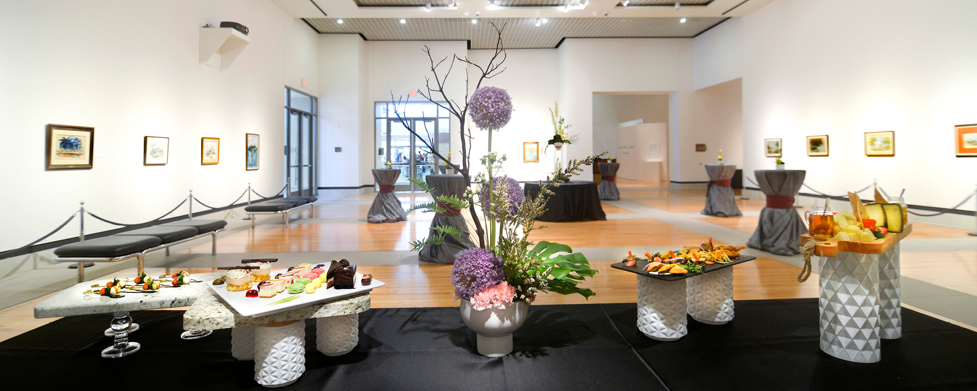 Gallery space set up with a reception table and bistro tables. 