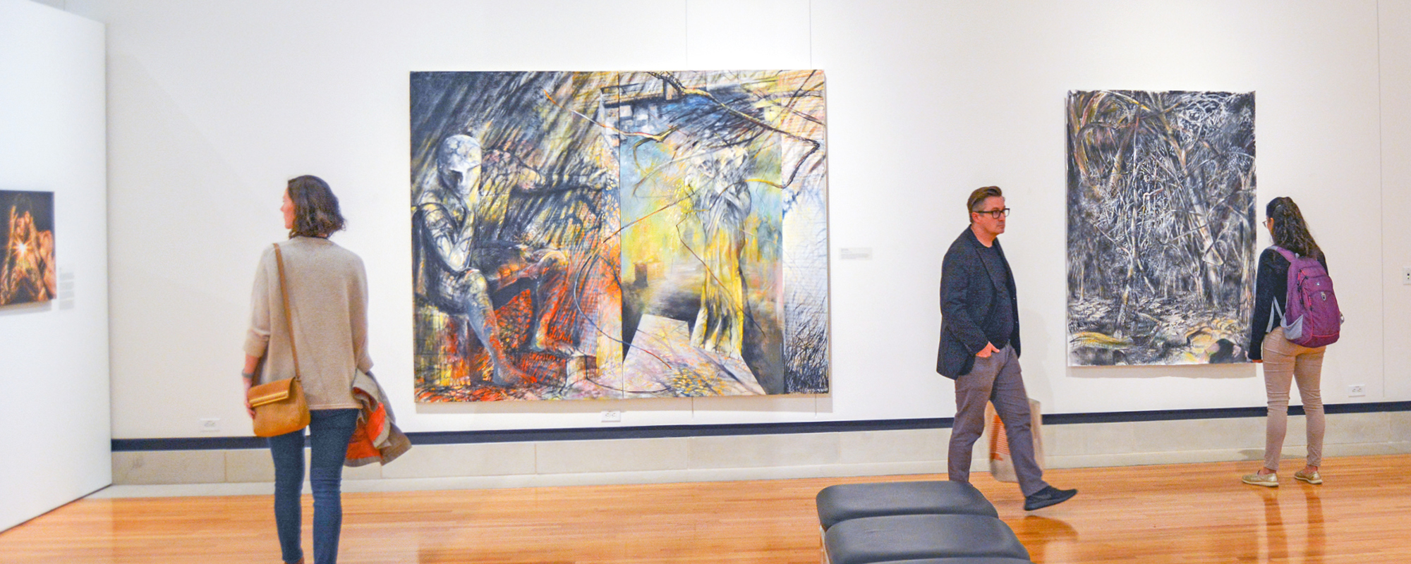 Visitors look at art hanging on gallery walls.