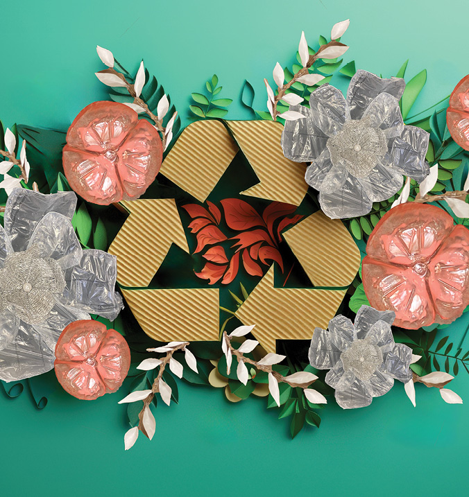 Cardboard recyle symbol surrounded by flowers made of paper, water bottles and bubble wrap