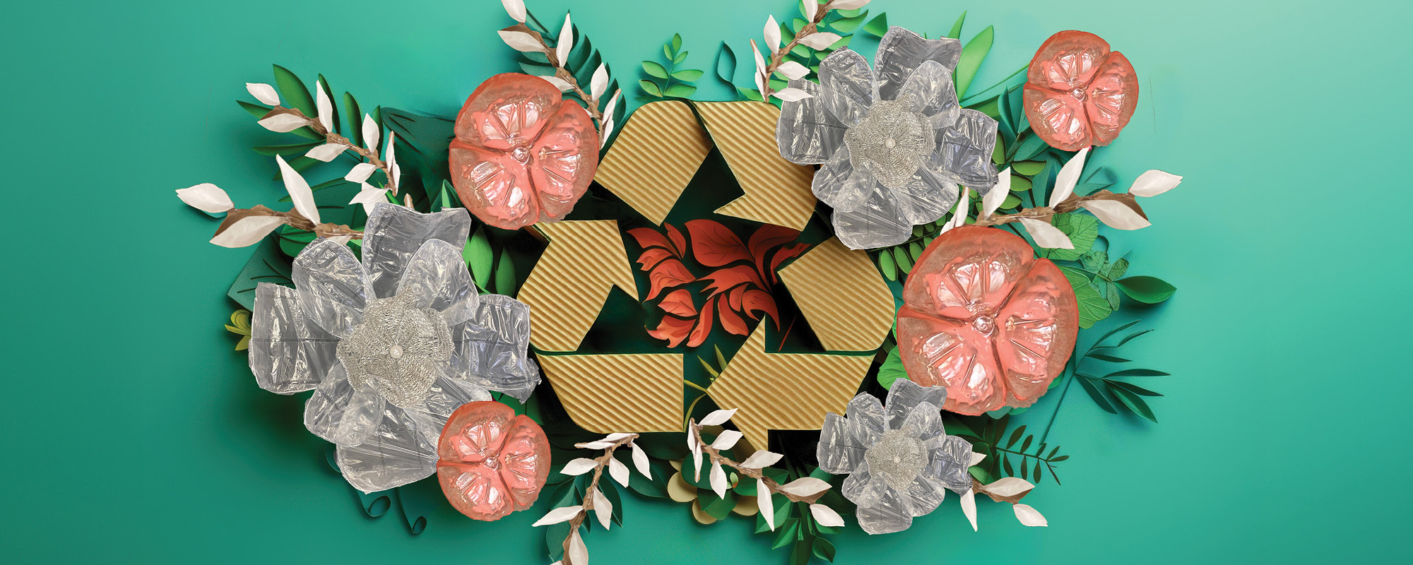 Cardboard recyle symbol surrounded by flowers made of paper, water bottles and bubble wrap
