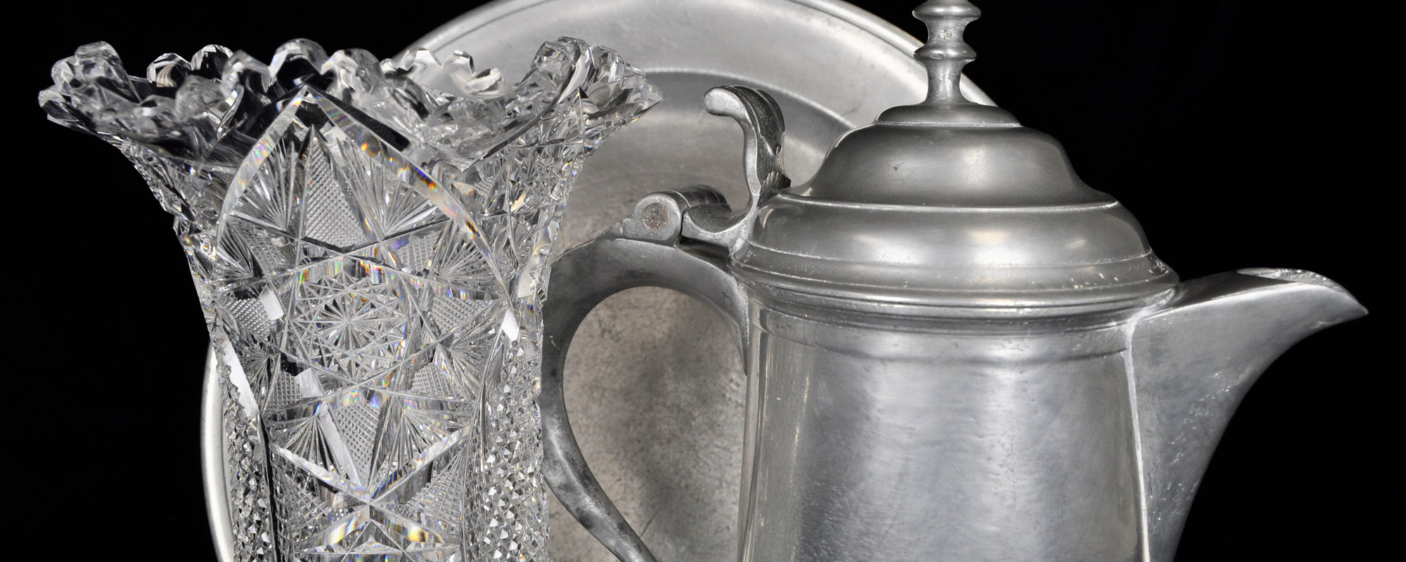 A pewter plate and flagon next to a crystal glass vase