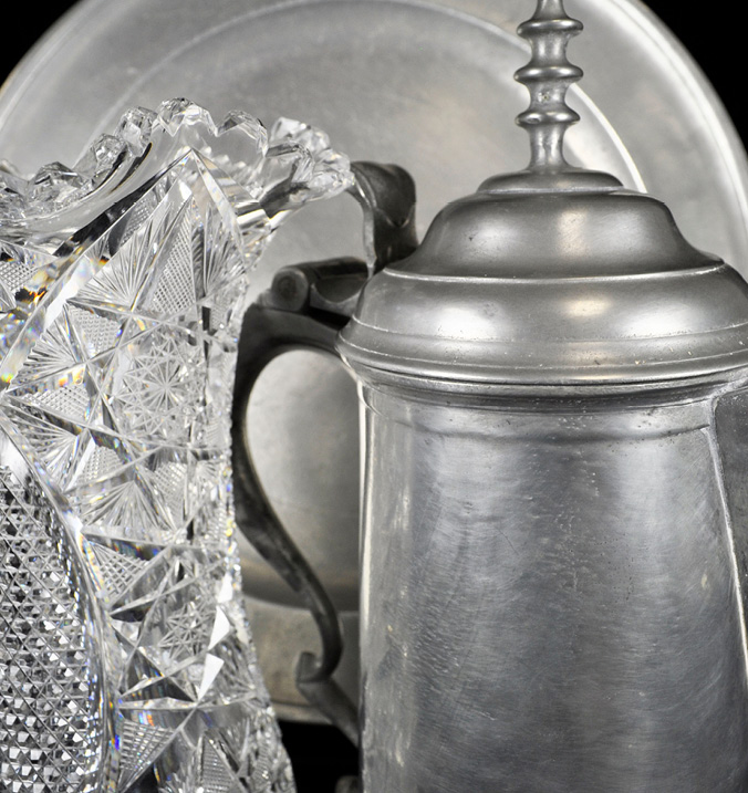 A pewter plate and flagon next to a crystal glass vase